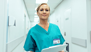 a nurse in green scrubs holding a clipbioard in a hospital corridor 