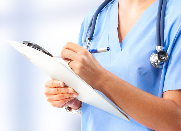 a nurse in blue scrubs writing on a white clipboard